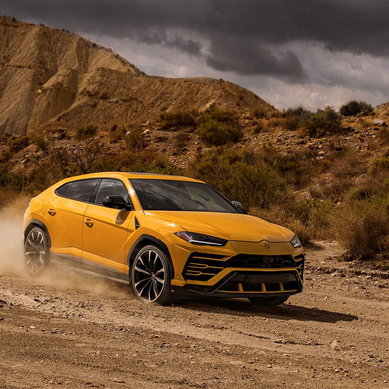 Yellow Lamborghini Urus driving in the middle of the desert.