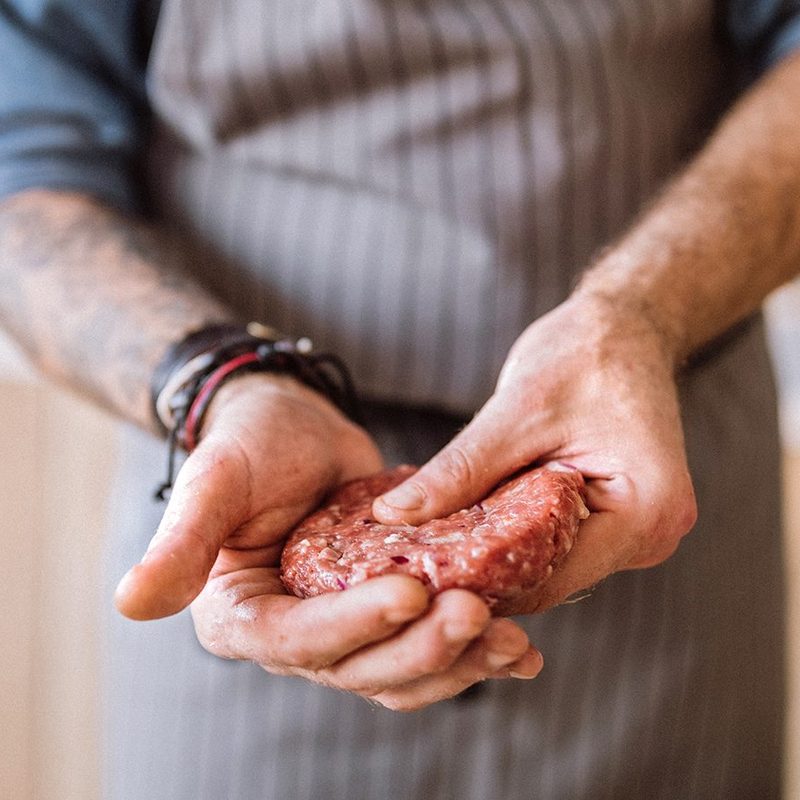 Holding a seasoned burger patty