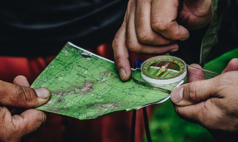 Fingers holding a map and compass in the outdoors