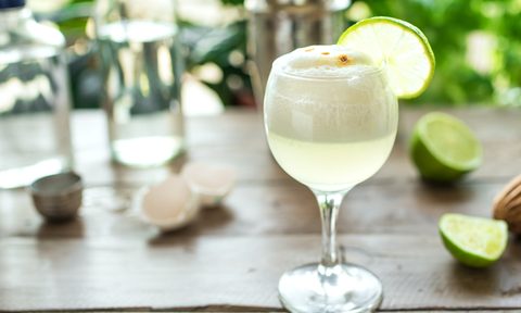 A cold glass of Pisco sour cocktail with lime on a wooden table