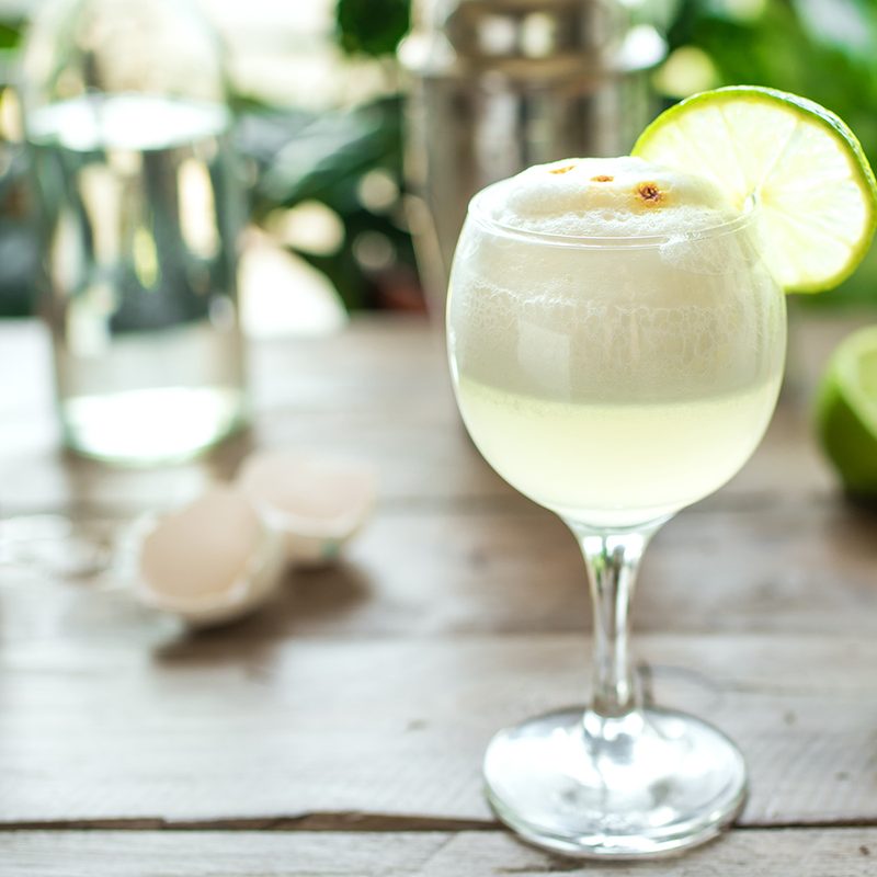 A cold glass of Pisco sour cocktail with lime on a wooden table