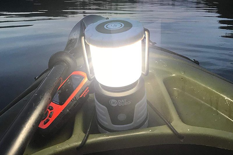 An illuminated UST Duro 30-Day LED Camping Lantern on a kayak on a body of water.