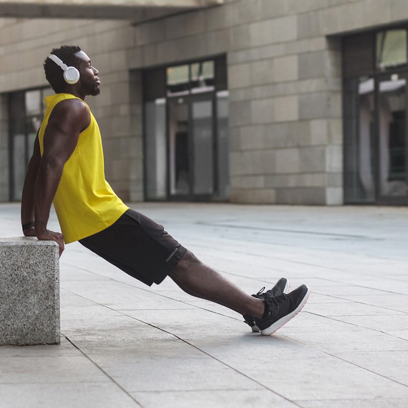 Man leaning against a concrete block doing dips.