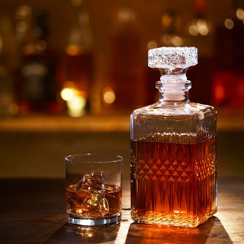 A decanter filled with bourbon sits next to a glass of bourbon and ice.