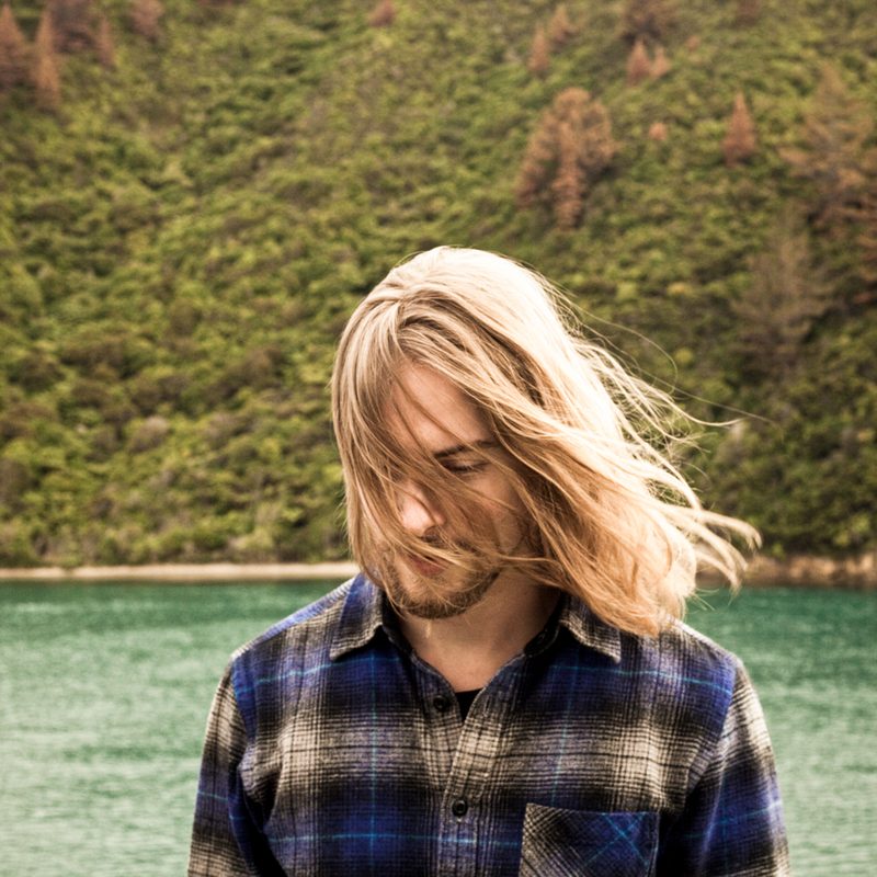Man with long blonde and wavy hair at the beach.
