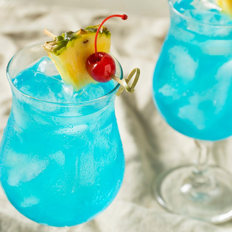 Blue Hawaiians garnished with a cherry and a slice of pineapple on top.
