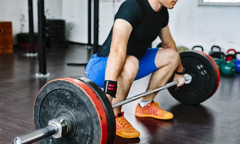 A man wearing a black shirt as he does a deadlift in the gym
