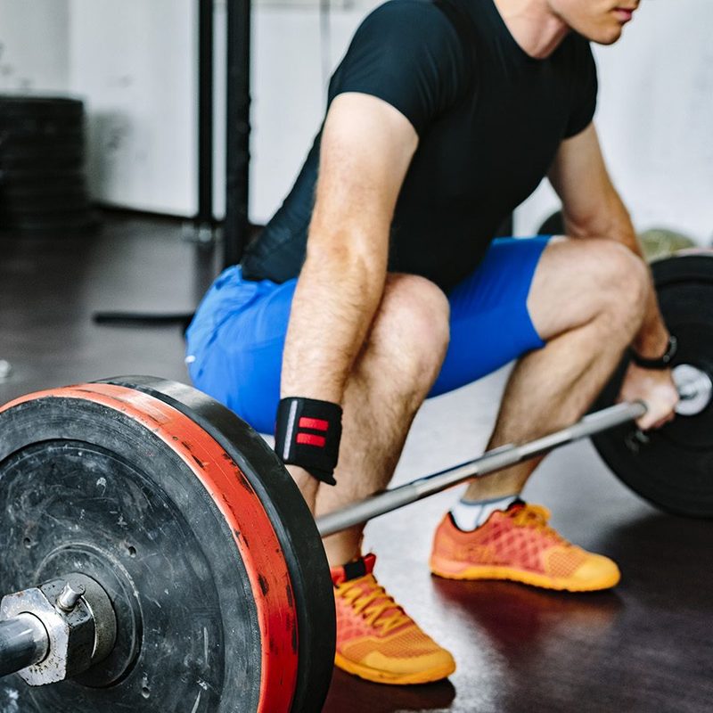 A man wearing a black shirt as he does a deadlift in the gym.
