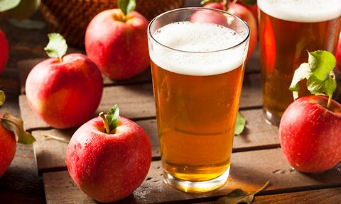 Hard apple cider in a glass, surrounded by apples.