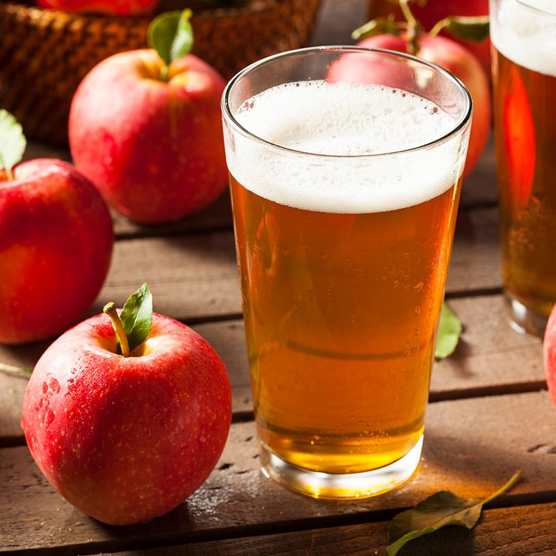 Hard apple cider in a glass, surrounded by apples.