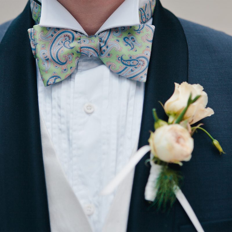 Torso of a man wearing a tuxedo jacket, formal shirt, paisley tie, and a boutonniere.