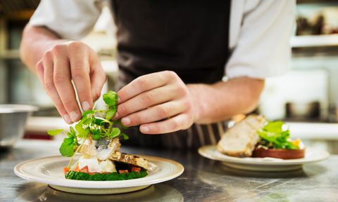 Close up of chef in kitchen adding salad garnish to a plate with grilled fish.