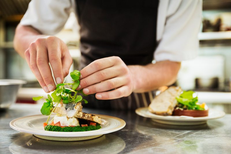 Close up of chef in kitchen adding salad garnish to a plate with grilled fish.