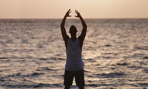 man stretching beach sun