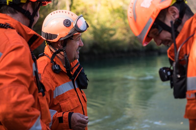 Three people from an emergency team discussing rescue operations near a body of water.