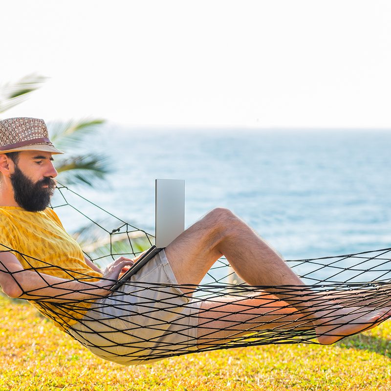 Man working on a laptop from a hammock by the ocean.