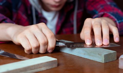 A young man sharpening a knife using a whetstone.