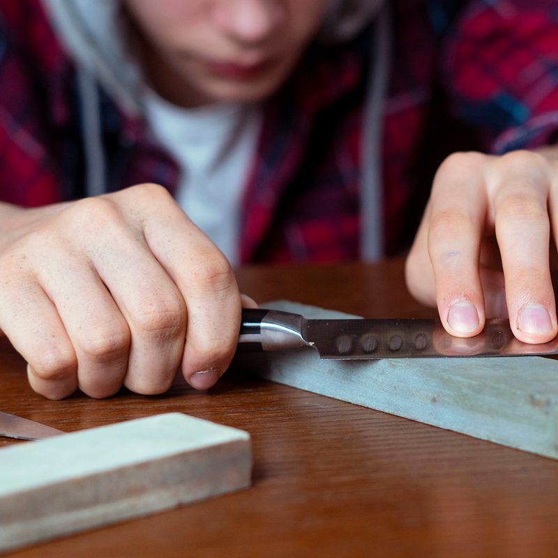 A young man sharpening a knife using a whetstone.