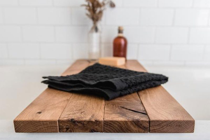 A black towel and other bathroom essentials on a Peg and Awl Bathtub Caddy.