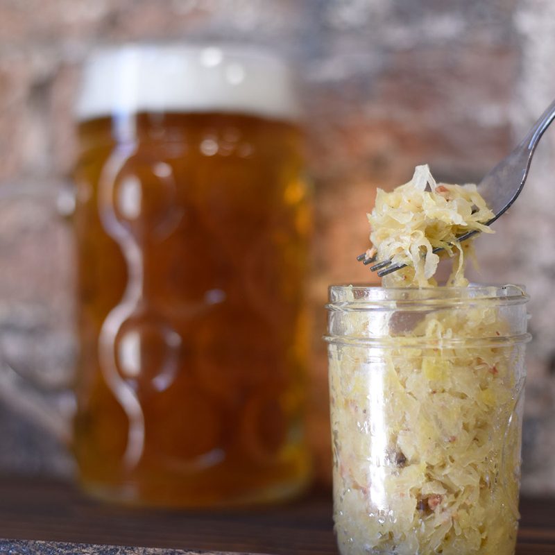 person with a fork picking up sauerkraut from a jar with a mug of beer in the background.