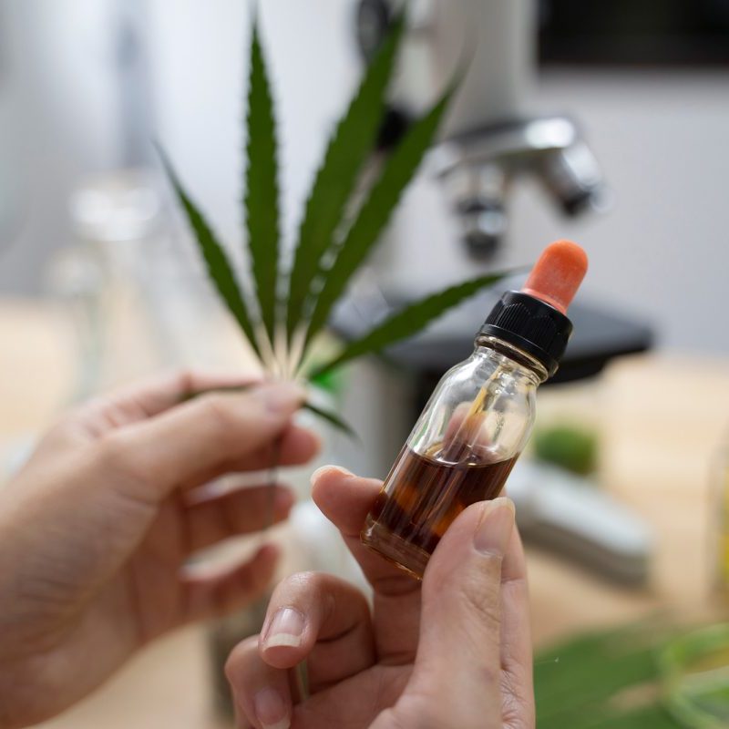 Someone holding a vial of CBD oil and a leaf in the other hand.