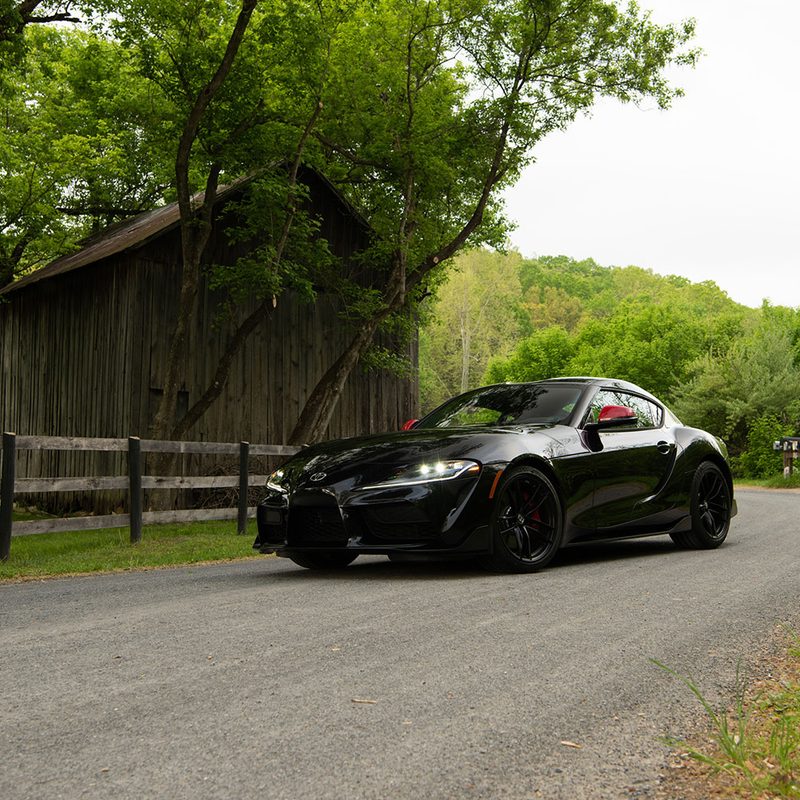 Toyota GR Supra front end angle from driver's side parked on the side of the road in front of an old barn.