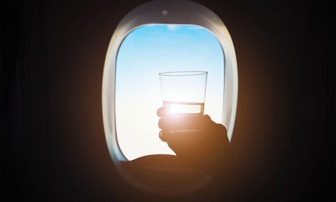 Person holding a drink on a plane with sunlight in the background