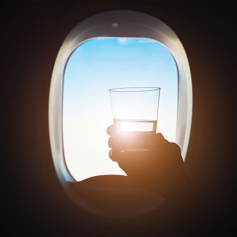 Person holding a drink on a plane with sunlight in the background