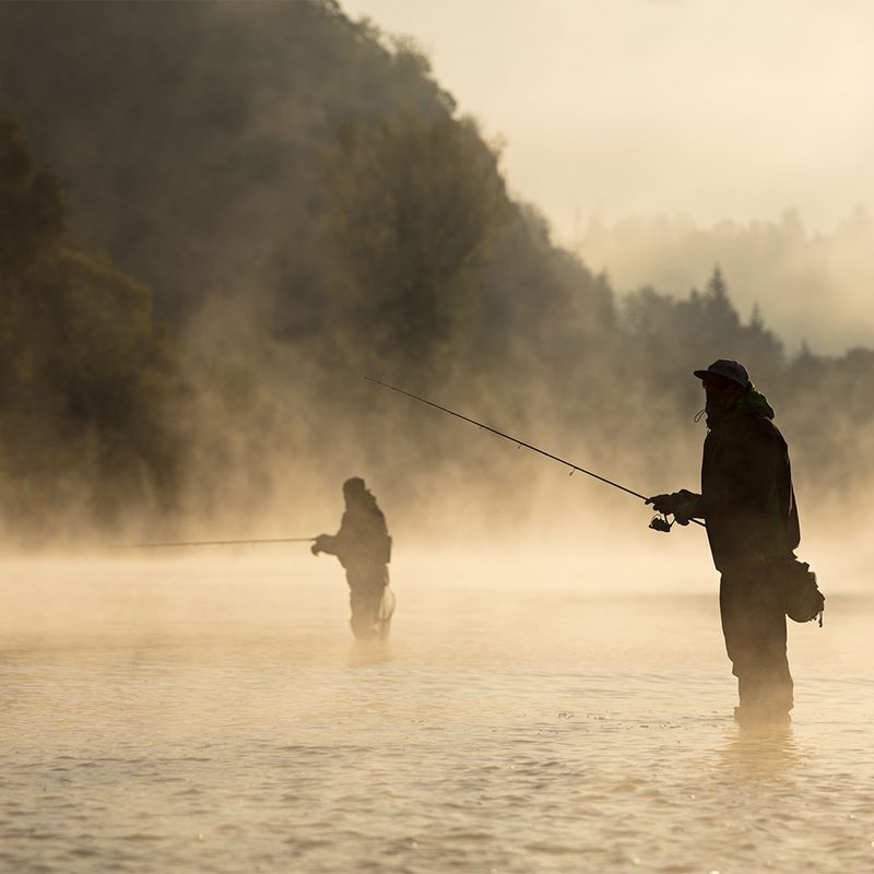 Two men fly fishing in a river shrouded in mist and fog