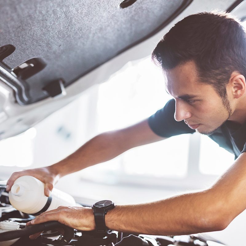 Close-up of an adult man changing the oil of his vehicle.