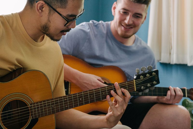 Man learning how to play the guitar from his friend.