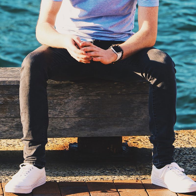 A man sitting on a concrete seat, wearing white sneakers.