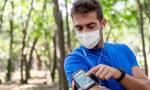 Man running outdoors wearing a facemask and using an arm band for his cell phone