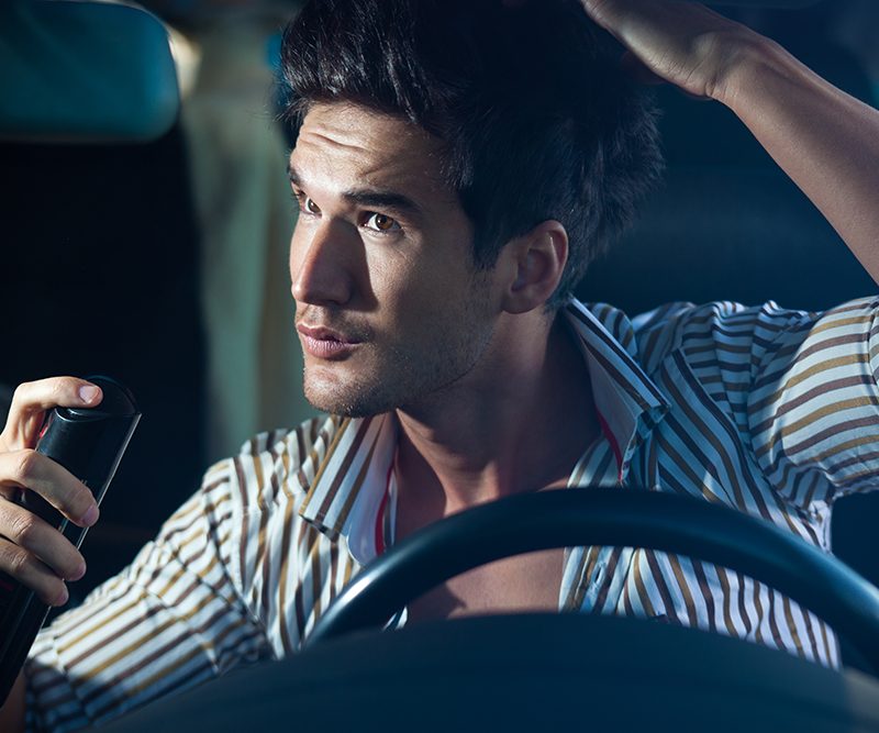A man using dry shampoo inside a car.