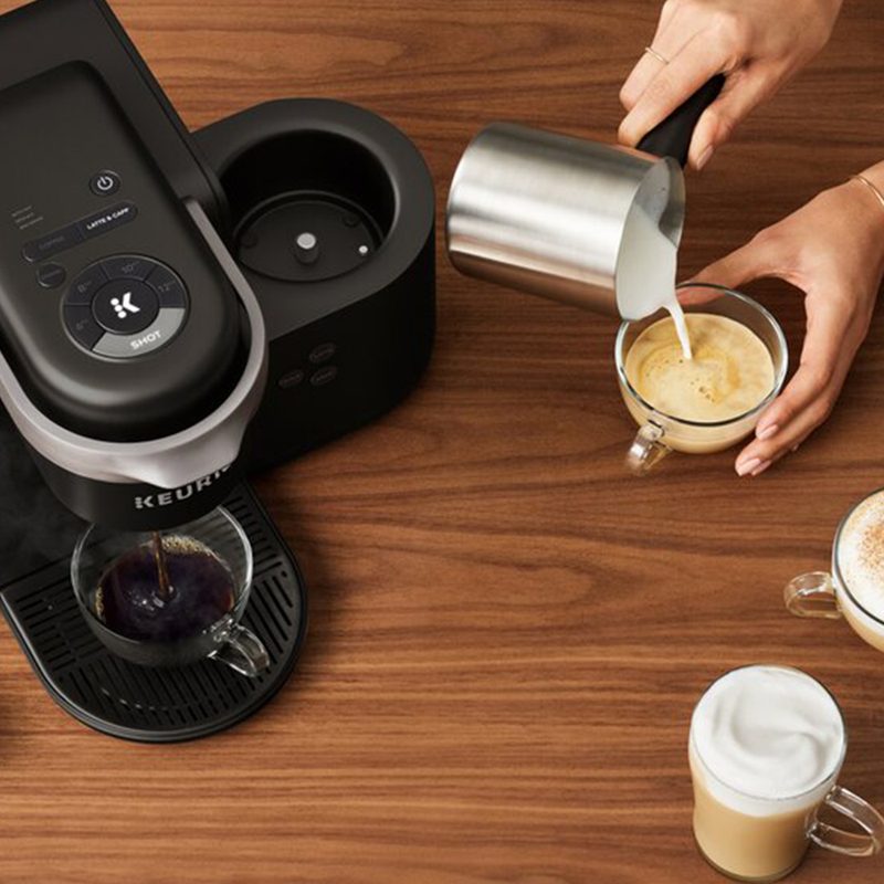 Keurig K Cafe brewing coffee with a woman pouring milk into a coffee cup.