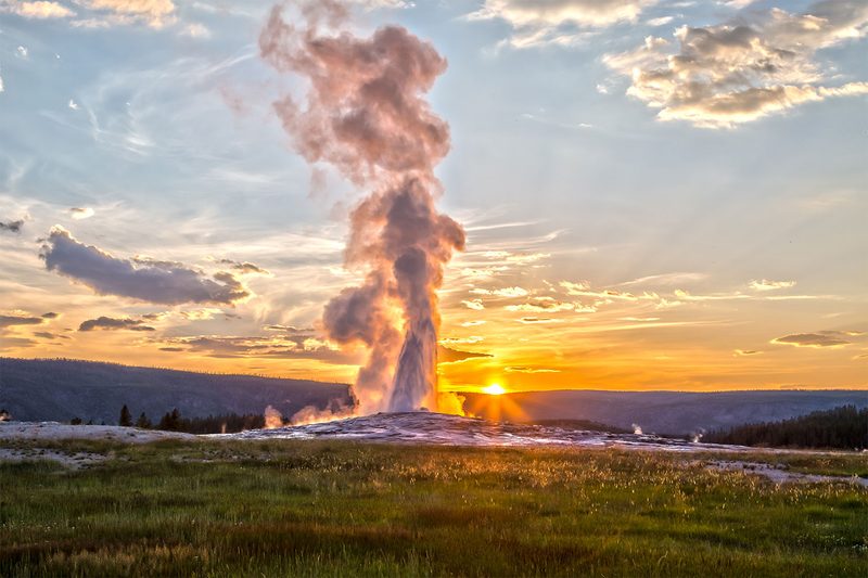 Old Faithful geyser eruption in Yellowstone National Park at sunset.