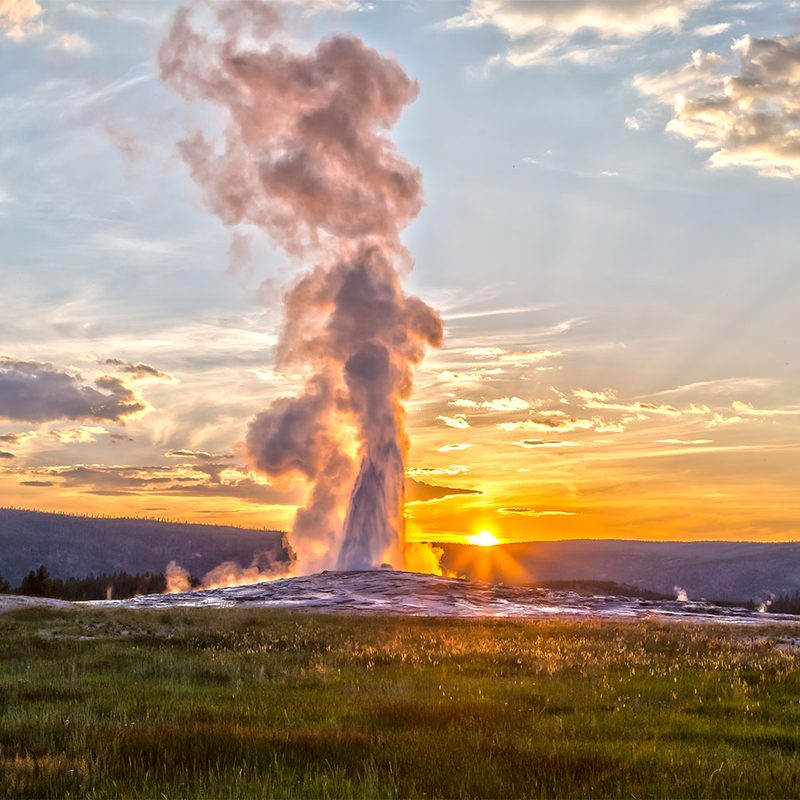 Old Faithful geyser eruption in Yellowstone National Park at sunset.