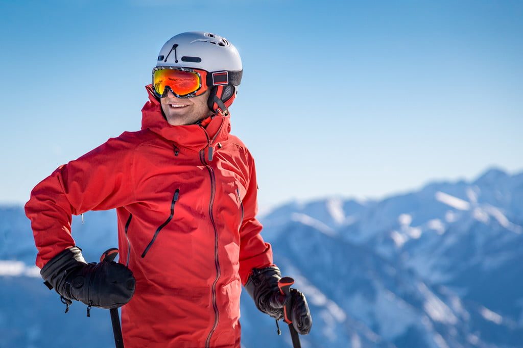 Smiling nan in a red ski jacket and helmet standing on a ski slope.