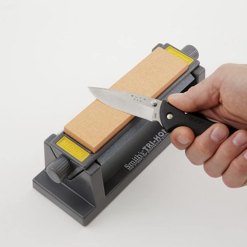 Hand of a man holding a knife against a sharpening stone.