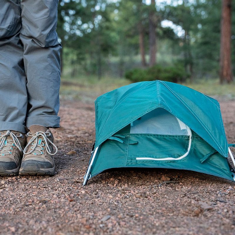 A Tiny Tent beside a person's legs in the forest.