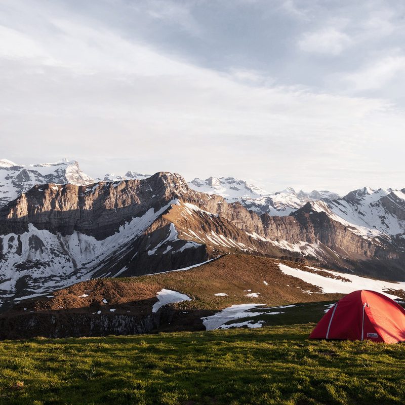 A camping tent on a grassy field near snowy mountains.