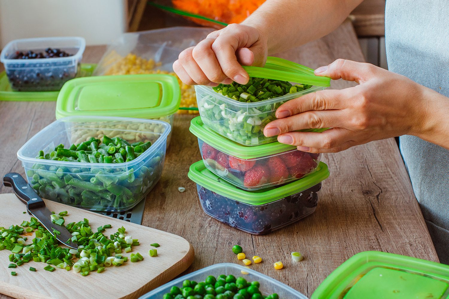 A hand opening the lid of a meal prep container on a kitchen table