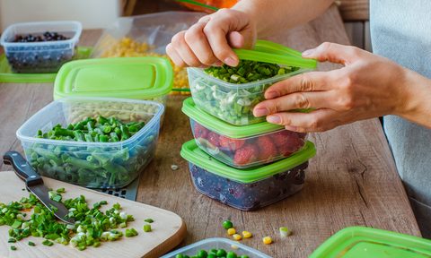 A hand opening the lid of a meal prep container on a kitchen table