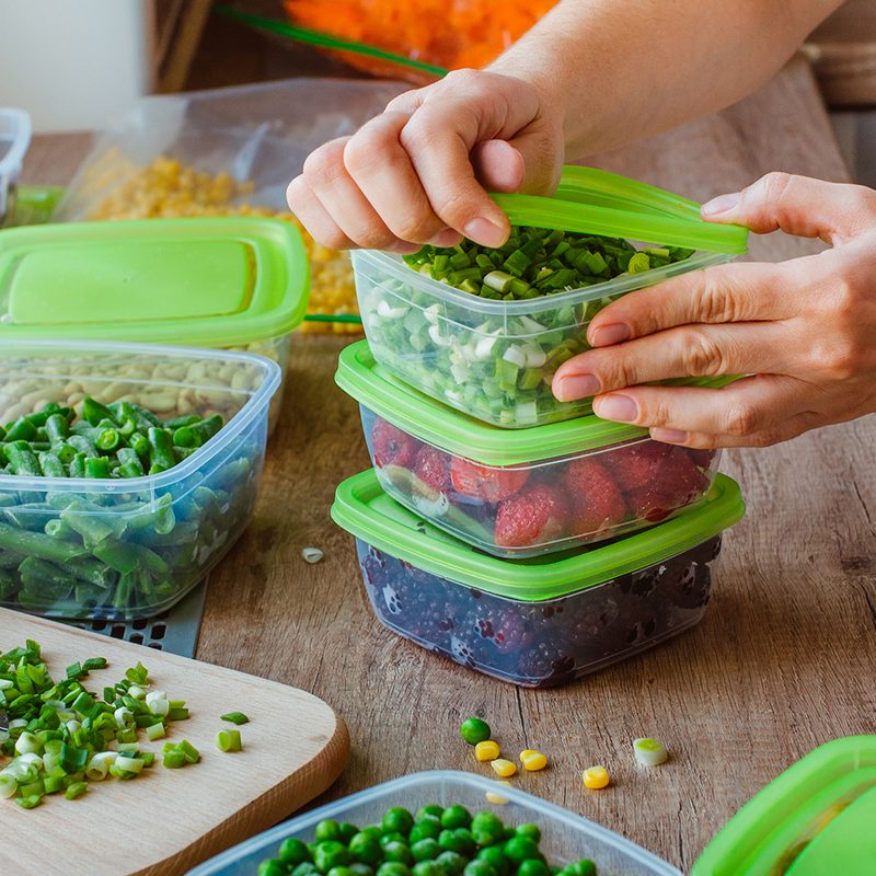 A hand opening the lid of a meal prep container on a kitchen table