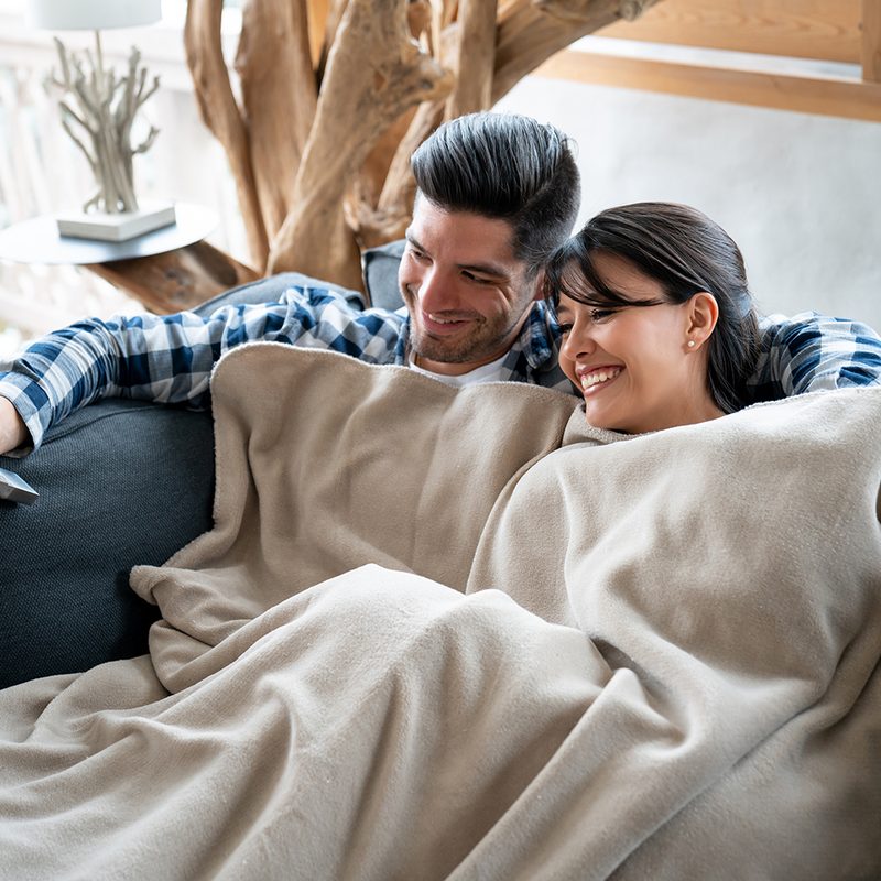 man and woman lying on a couch with a blanket.