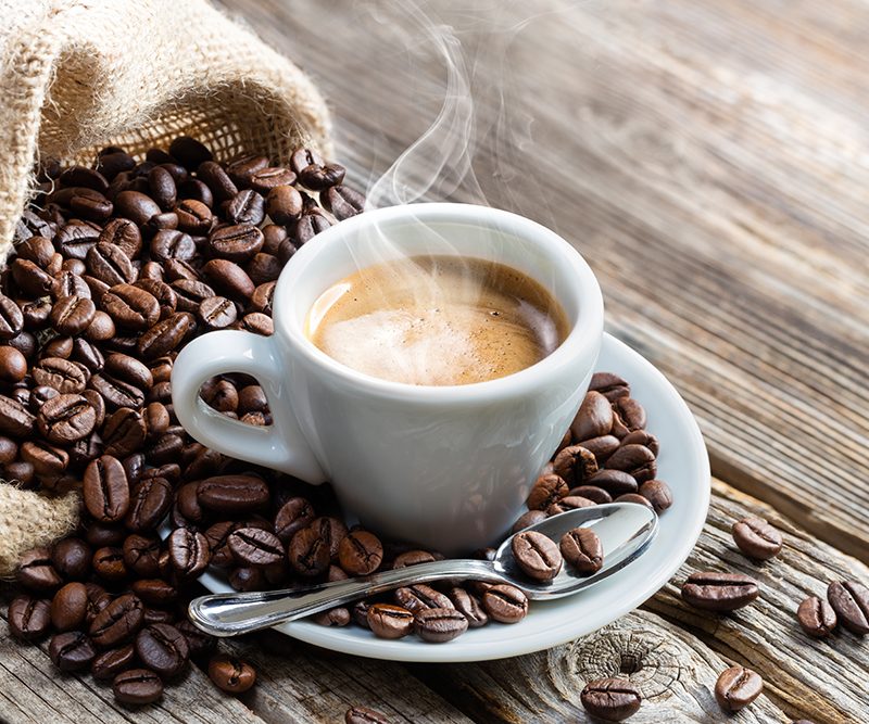 A warm cup of coffee and spoon on a saucer with coffee beans
