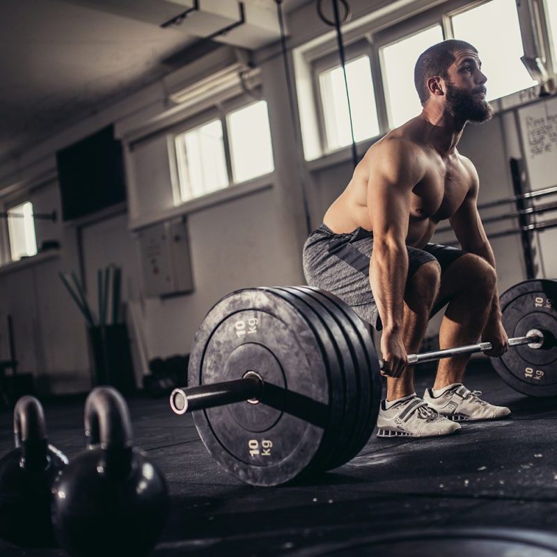 Man with a buzzcut at an empty gym preparing to do a sumo-style dead lift.
