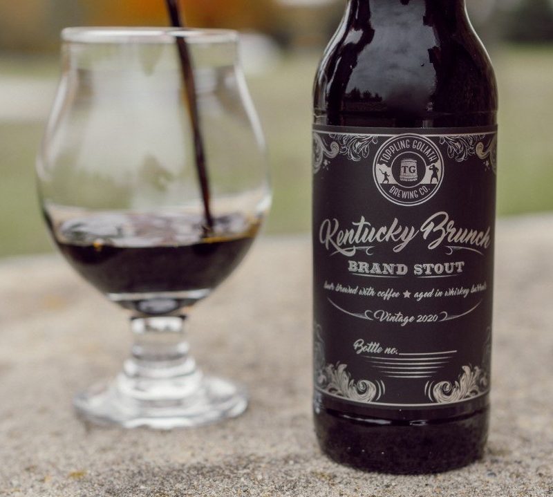 A bottle of Toppling Goliath Stout and a glass containing the said beer displayed on a hard surface.