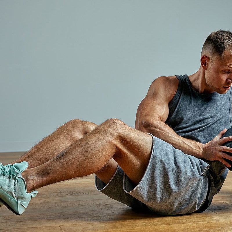 A man doing a Russian Twist while holding a medicine ball.