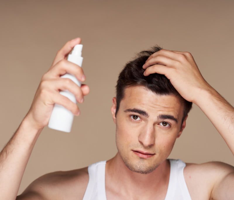 A man spraying a hair product into his hair.